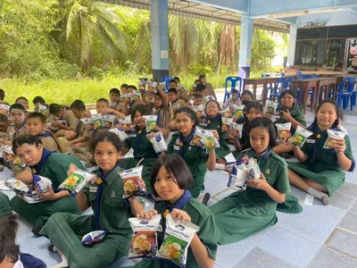 นักเรียนโรงเรียนประถมศึกษารับขนมเทมเป้ทอดกรอบที่วัดจุฬามณีมอบให้
